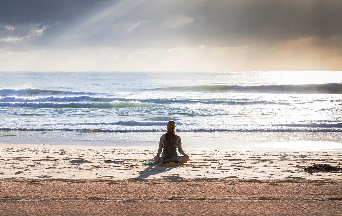 A woman mediates alone on a beach in the morning sun