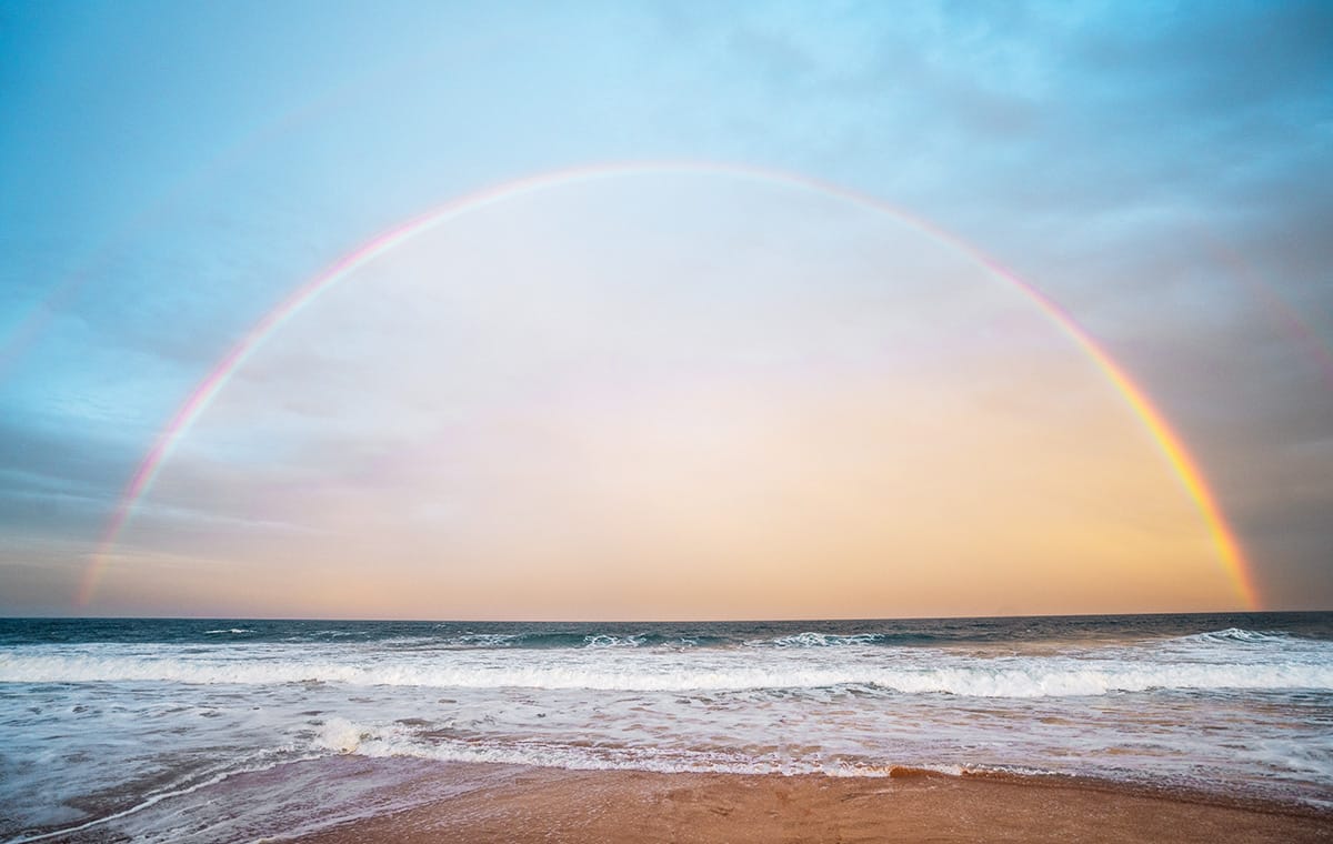 A rainbow forms over crashing waves at a beach